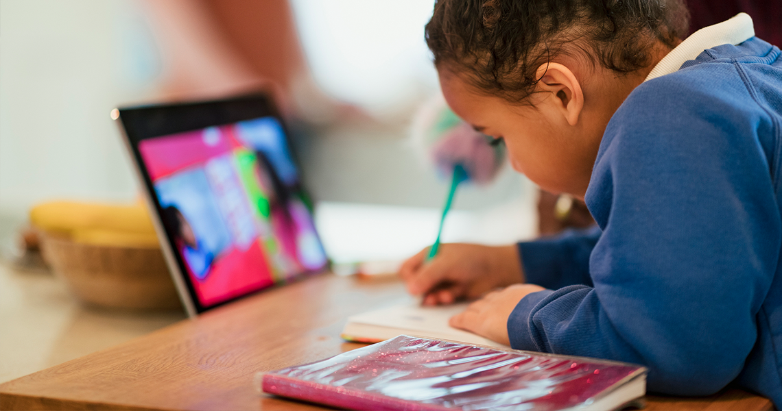 young student working with pencil, notebook, and ipad at kitchen table