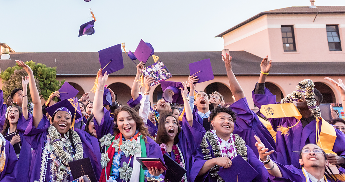 group of students in graduation gowns, throwing their caps