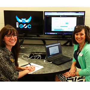 two women sitting at a desk in front of a computer