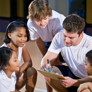 students surrounding a coach who is giving instructions from his clipboard