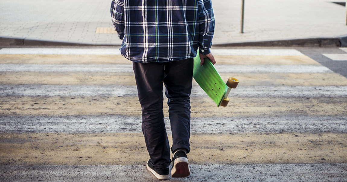 a boy crossing the street with a skateboard. A cut curb on the other end