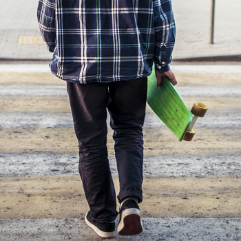 a boy crossing the street with a skateboard. A cut curb on the other end