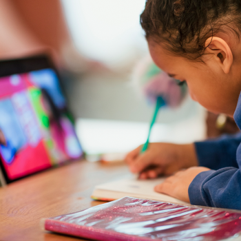 young student working with pencil, notebook, and ipad at kitchen table