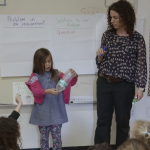 Teacher working with young student in front of class